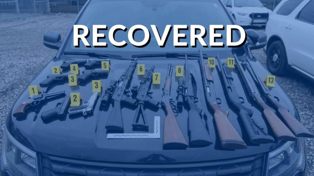 A collection of recovered firearms, including handguns, rifles, and shotguns, displayed with yellow evidence markers on the hood of a police patrol vehicle, with the word "RECOVERED" overlaid in large white text.